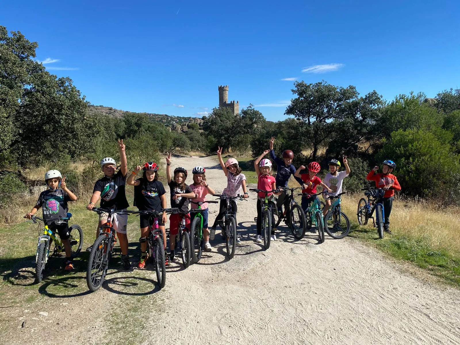 Un grupo de alumnos con sus bicicletas en un camino de la sierra, con una torre al fondo.