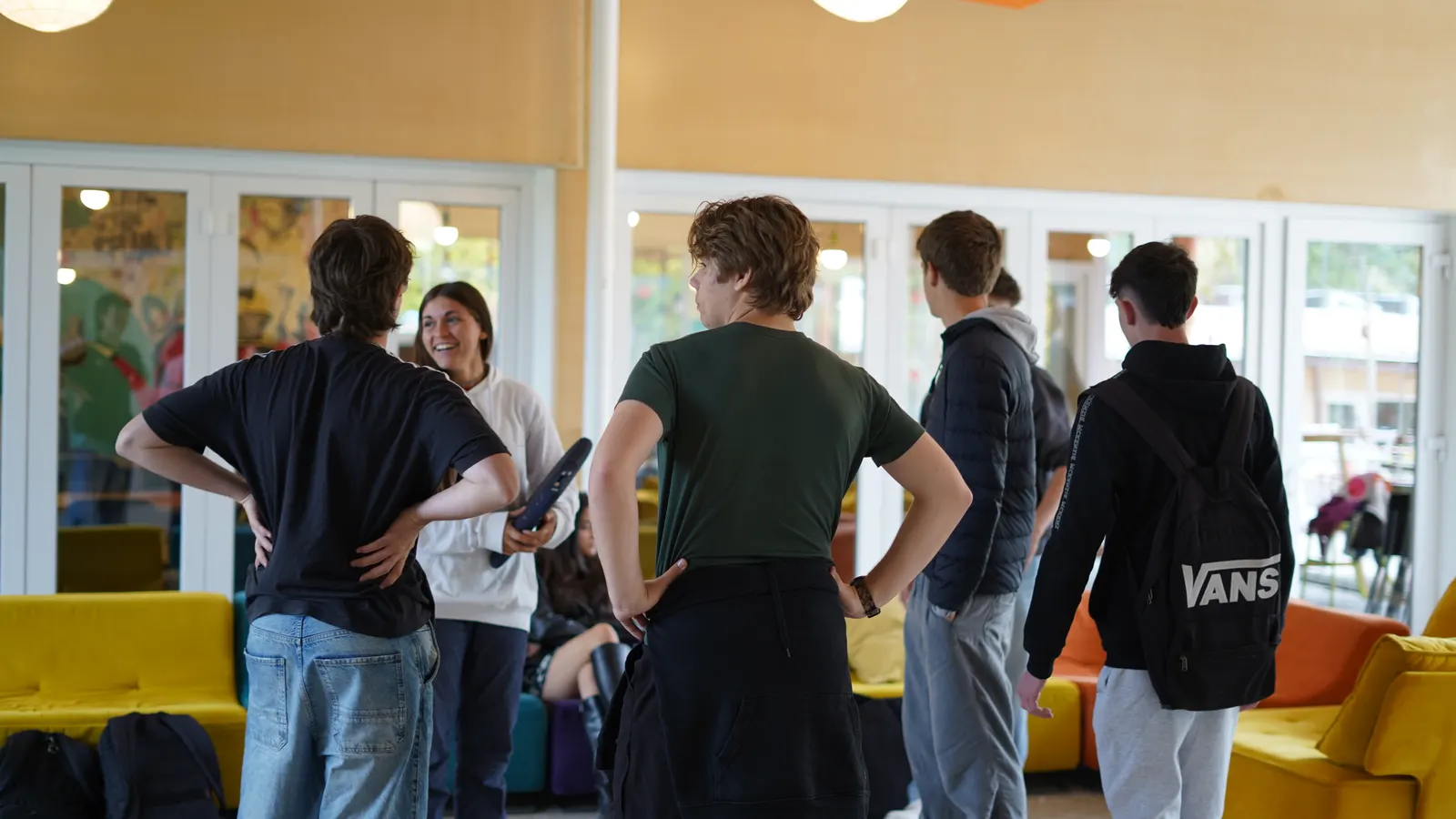 Un grupo de alumnos de secundaria conversa de pie en un aula luminosa, junto a una profesora.