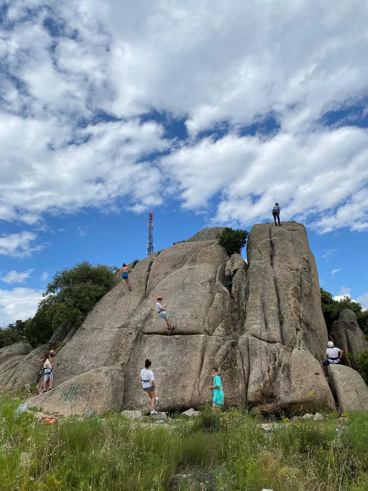 Un grupo de alumnos escala una formación rocosa de la sierra de Guadarrama bajo un cielo despejado.